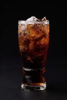 Cola en vaso con cubitos de hielo transparente aislado sobre fondo negro foto