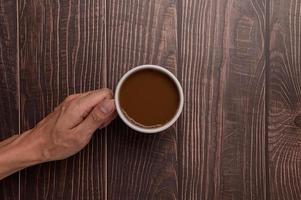 Hand holding a coffee mug on a wood background photo
