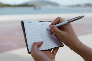 Woman hand writing down in small white memo notebook for take a note. photo