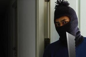 Masked robber with knife hiding behind the door photo