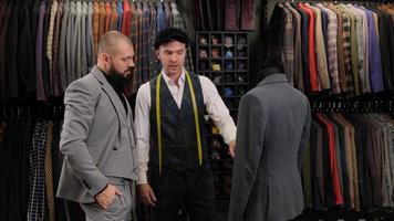 cámara lenta de hombre guapo eligiendo un diseño de traje con sastre en atelier. diseñador que presenta el traje del menequin al comprador