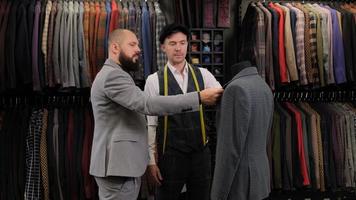 Slow motion of handsome man choosing a suit design with tailor in atelier. designer presenting the costume on the menequin to the buyer