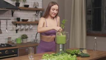 Sporty Woman making, pouring, drinking green vegetable smoothie with blender. Healthy eating lifestyle with young woman preparing blending smooithies drink with spinach, celery at home in kitchen. photo