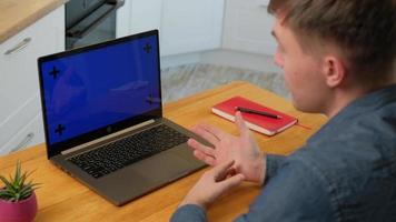 Vista izquierda del hombre inteligente hablando con un colega mientras realiza una videollamada en una computadora portátil con pantalla de croma mientras trabaja en casa. foto