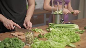 Man cuts fresh celery on a cutting Board at the home kitchen. Woman helping cooking vegetable cocktail