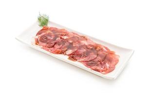 Carne de cerdo fresca en rodajas con salsa sobre fondo blanco.