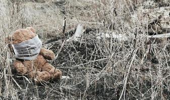 Oso de peluche en máscara médica sentado en la basura foto