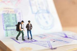 Miniature people couple standing on passport with immigration stamped photo