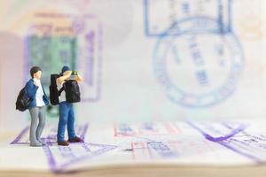 Miniature people couple standing on passport with immigration stamped photo