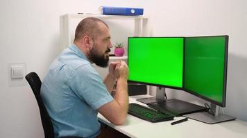 hombre escribiendo en el teclado en dos monitores con la pantalla verde. trabajo remoto en casa foto