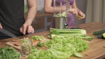 healthy eating, cooking, vegetarian food, dieting and people concept - couple of young peaple with blender and green vegetables making detox shake or smoothie at home.