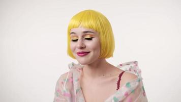 Closeup portrait of woman with colourful makeup in futuristic wearing at yellow wig light wall background. Girl has funny with a comb photo