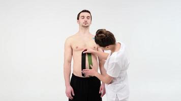 Terapeuta femenina aplicando cinta de kinesiología en el abdomen de un hombre sobre el fondo claro. Mujer prepara paciente masculino para pegar cinta adhesiva de kinesio en su vientre