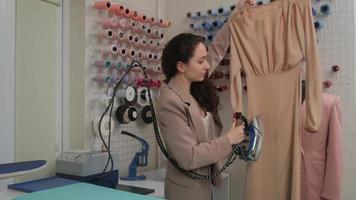 una modista vaporiza un nuevo vestido a medida con una plancha de vapor especializada en un taller de costura. el proceso de coser ropa nueva.