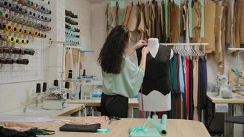 costurera está midiendo la ropa en sastrería maniquí con cinta métrica. la mujer está concentrada y pensativa. El estudio es ligero, moderno, con muchas herramientas y artículos de costura.