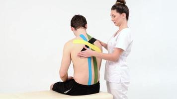 Physiotherapist sticks kinesio tapes to the back of patient, kinesiology taping, kinesiological therapy, athlete are recovering after injury of loins, 4k