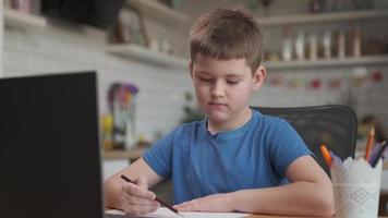 niño inteligente usa una computadora portátil para una videollamada con su maestro. la pantalla muestra una conferencia en línea con el maestro explicando el tema de un aula, el niño escribe información.