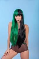 portrait of young woman wearing green black halh color wig, black lips makeup, clean skin. blue backgound. photo