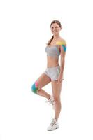 Kinesiology taping. Young female athlete isolated on white background with kinesiology tape on shoulder and knee. Fat lose, sport physical therapy,recovery concept.