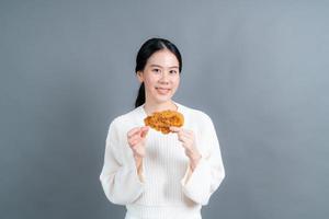 Young Asian woman wearing t-shirt with happy face and enjoy eating fried chicken on grey background photo