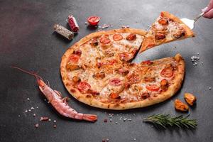 Sabrosa pizza en rodajas con mariscos y tomate sobre un fondo de hormigón foto