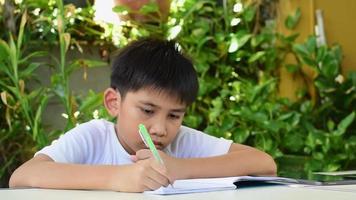 niño asiático haciendo sus deberes con un bolígrafo para escribir en un cuaderno.