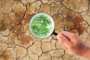 Hand holding magnifying glass to find a leaf on dry cracked earth photo