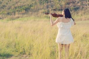 Bella mujer de pie tocando el violín en la pradera foto