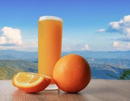 Vaso de jugo de naranja sobre un fondo de madera con montañas y cielo azul foto