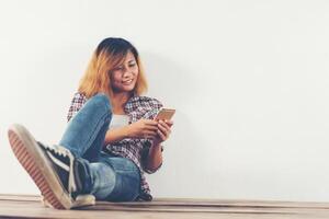 Feliz joven inconformista mujer sentada sobre un piso de madera escribiendo en el teléfono inteligente foto