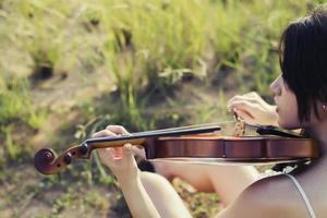 hermosa mujer sentada tocando el violín en la pradera foto