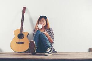 mujer joven inconformista tomando café chillin con guitarra sentada. foto