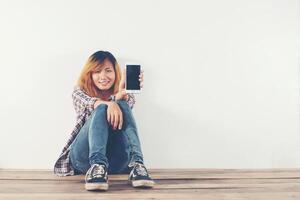 Happy young hipster woman sitting on wooden floor typing on smartphone photo