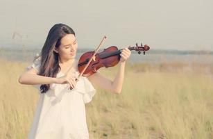Bella mujer de pie tocando el violín en la pradera foto