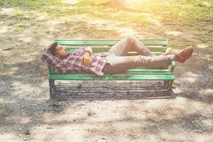 Young hipster man lying down on green park bench, looking away. photo