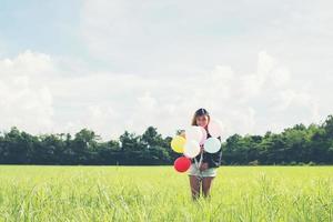 Happy young beautiful woman and colorful balloons in grassland. photo