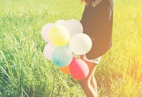 Happy young beautiful woman and colorful balloons in grassland. photo