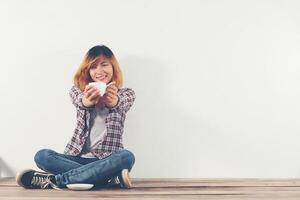 Feliz mujer sentada sobre un piso de madera con taza de café aislado sobre fondo blanco. foto