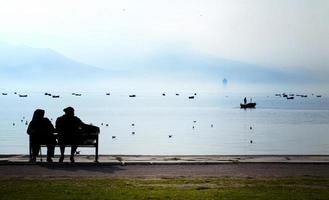 Seascape View and Silhouette Couple Sitting on a Wooden Seat photo