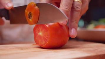 une main de femme utilisant un couteau de cuisine pour couper une tomate mûre sur du bois video