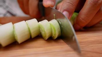 eine weibliche Hand mit einem Messer, um japanische lange Zwiebeln zu schneiden