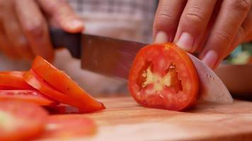 La mano de una dama con un cuchillo de cocina para cortar el tomate.