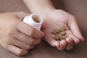 Medicina herbaria en pastilla en mano sosteniendo con botella blanca foto