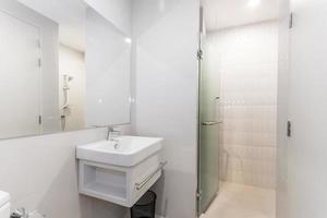 Baño blanco moderno y de madera con cabina de ducha de vidrio en el apartamento foto