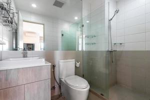 Baño blanco moderno y de madera con cabina de ducha de vidrio en el apartamento foto