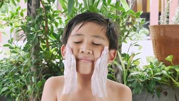 un garçon asiatique nettoie son visage avec un nettoyant moussant. video