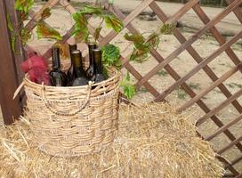 Botellas de vino en una canasta de paja sobre una pajita cerca de una celosía de madera