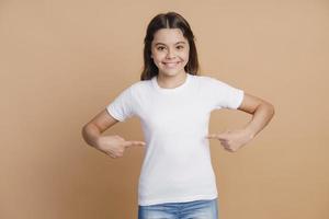 Positive, smiling teenage girl points to her white T-shirt photo