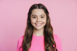 Smiling teenage girl sincerely smiling on a pink background photo