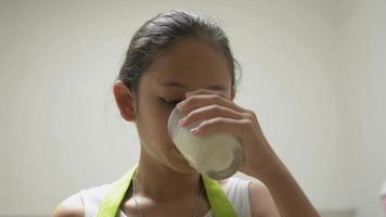 niña sana en delantal bebiendo una taza de leche en la cocina
